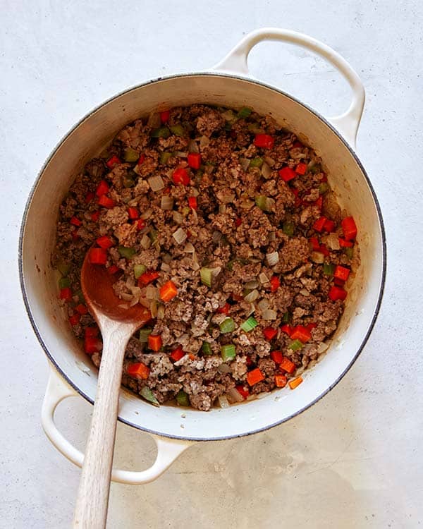 Beef, pork, and italian sausage in a pot with onions and celery to make bolognese sauce.
