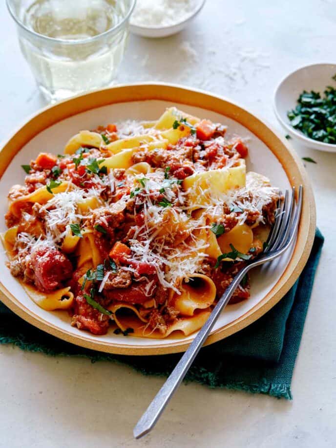 A bowl of bolognese sauce with a glass of wine in the background.