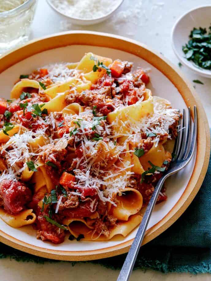 Bolognese sauce on pasta in a bowl with a fork in it and a glass of wine in the background.