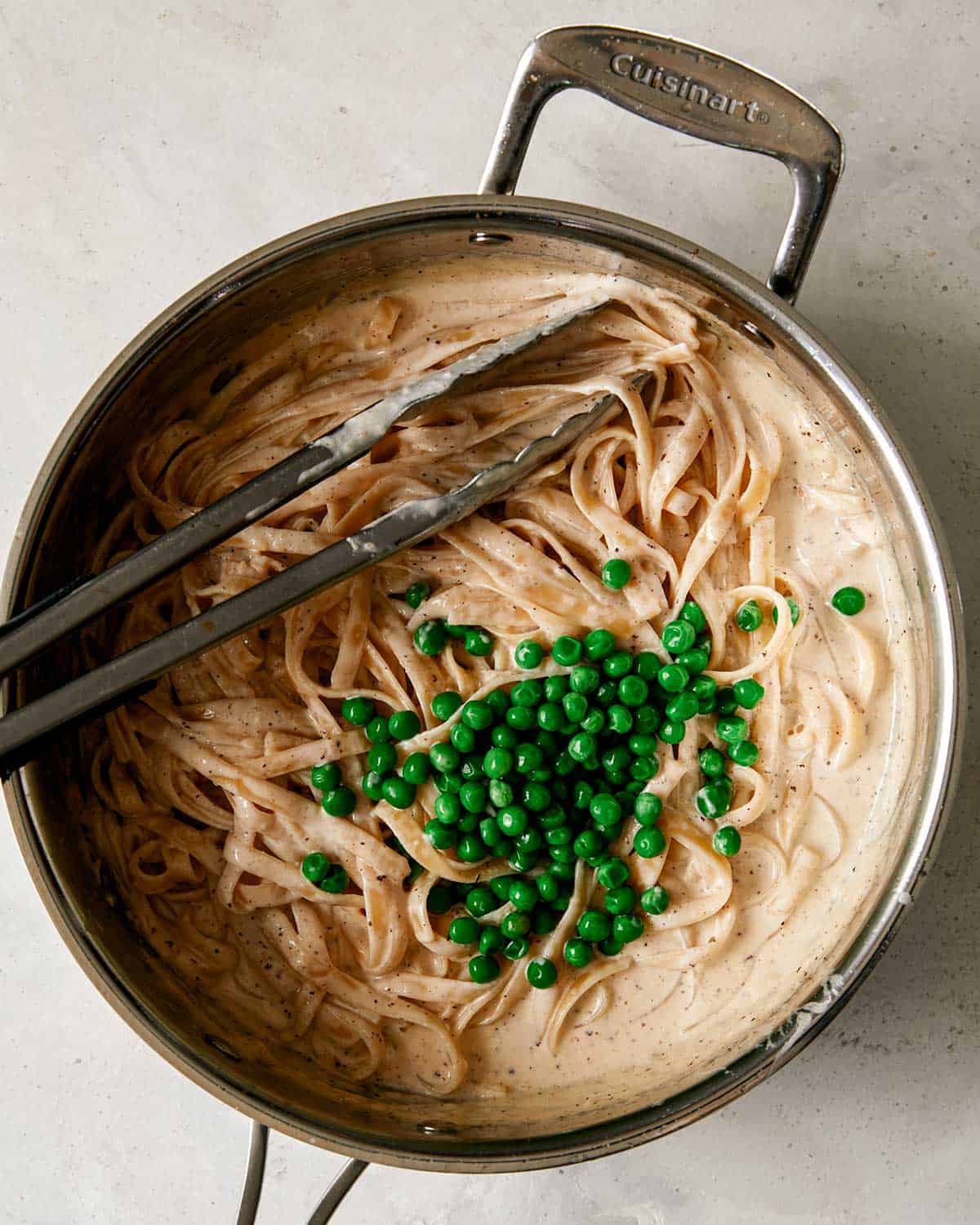 A skillet iwth browned butter fettuccine alfredo tossed with peas.