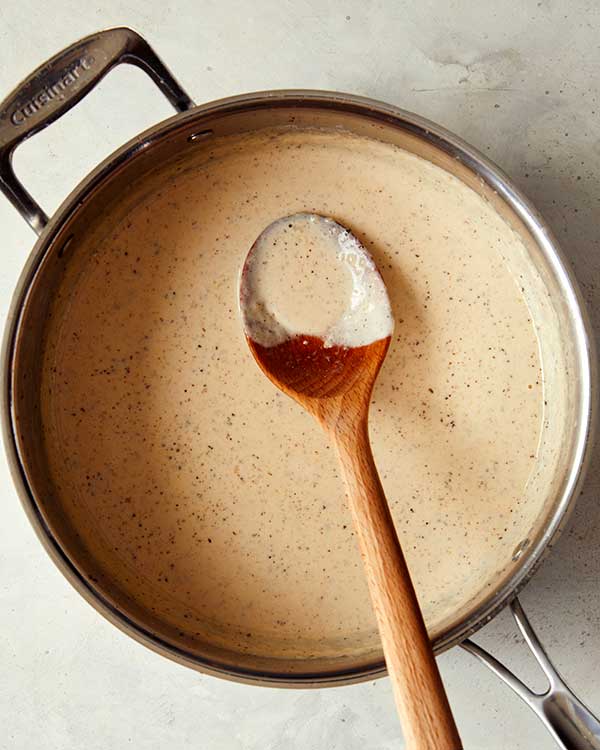 A skillet full of browned butter fettuccine alfredo sauce with a wooden spoon in it. 