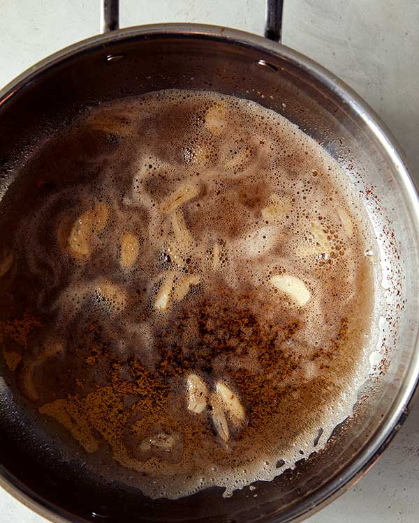 Thinly sliced garlic added into a skillet full of browned butter. 