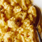 A bowl of cauliflower mac and cheese with a spoon.