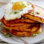 Cheesy Pumpkin Pancakes on a plate with a plate in the background of more pancakes.