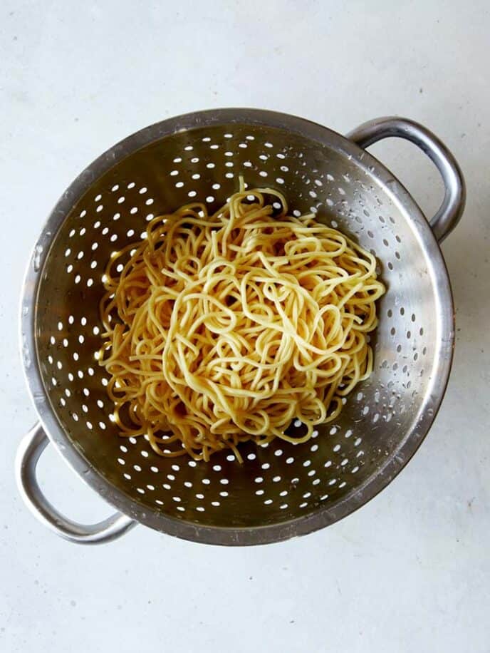 Chinese egg noodles in a collander after they have been cooked and drained. 