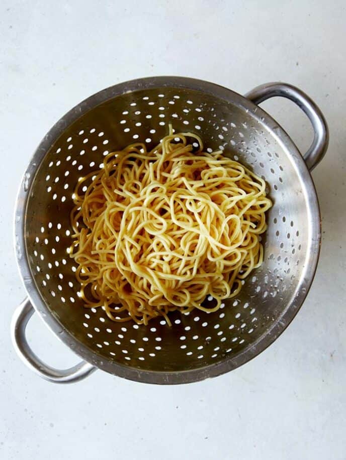 Chinese egg noodles in a collander after they have been cooked and drained.
