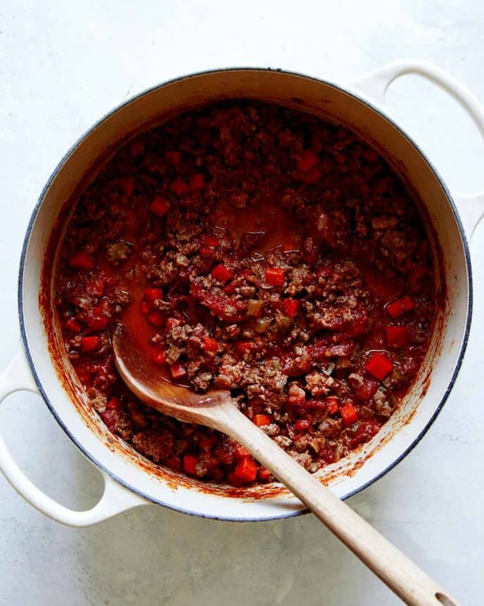 A big pot of bolognese sauce with a wooden spoon in it.