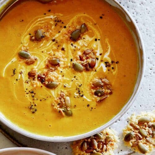 Creamy Pumpkin Soup recipe in a bowl with a spoon in it and parmesan crisps next to it, part of our Thanksgiving appetizers.