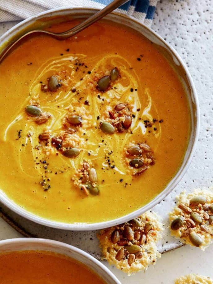 Creamy Pumpkin Soup recipe in a bowl with a spoon in it and parmesan crisps next to it.