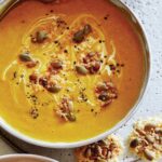 A bowl of Creamy Pumpkin Soup with parmesan crisps nearby.
