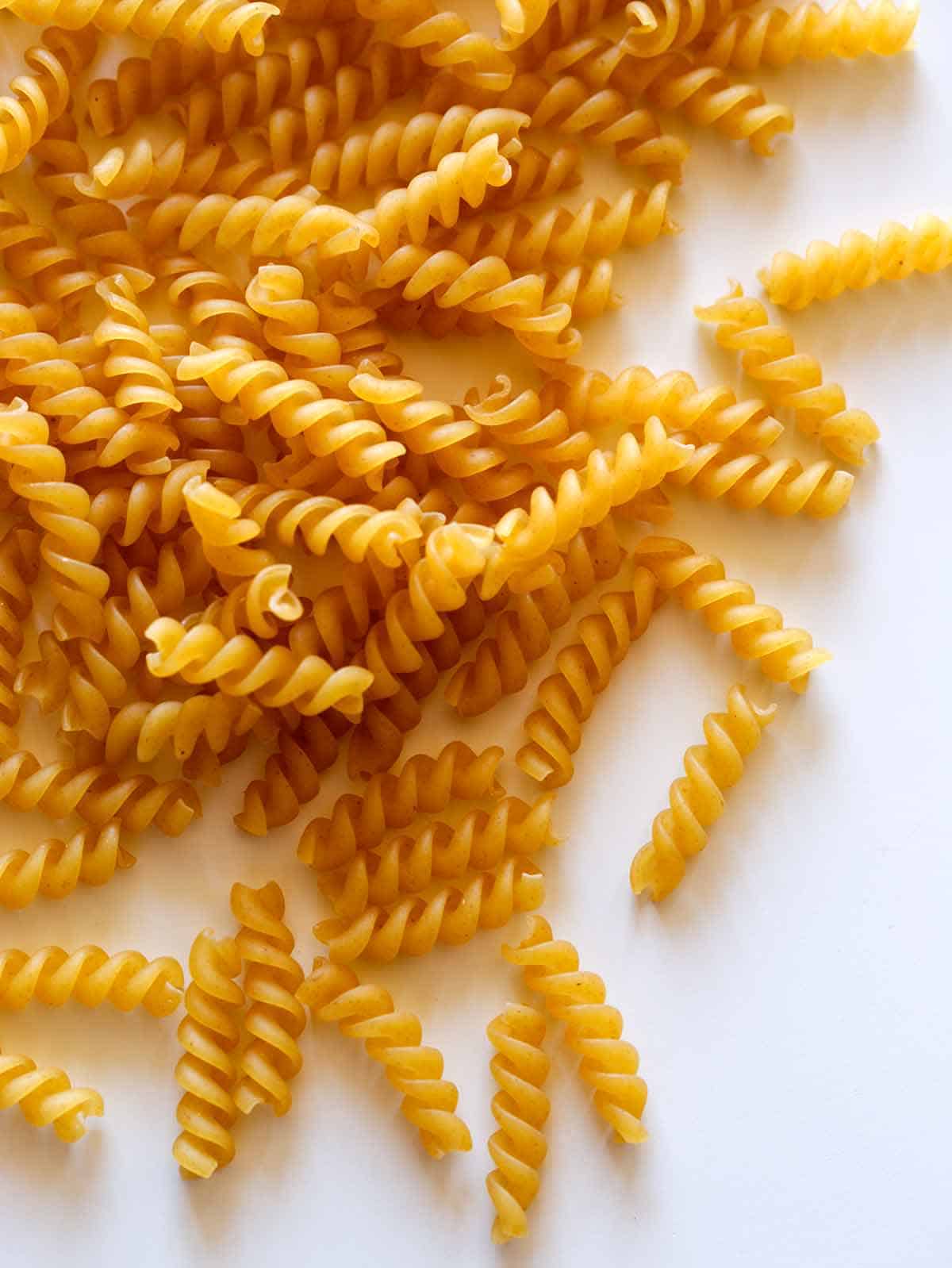 Raw and dried fusilli pasta spread out on a surface. 
