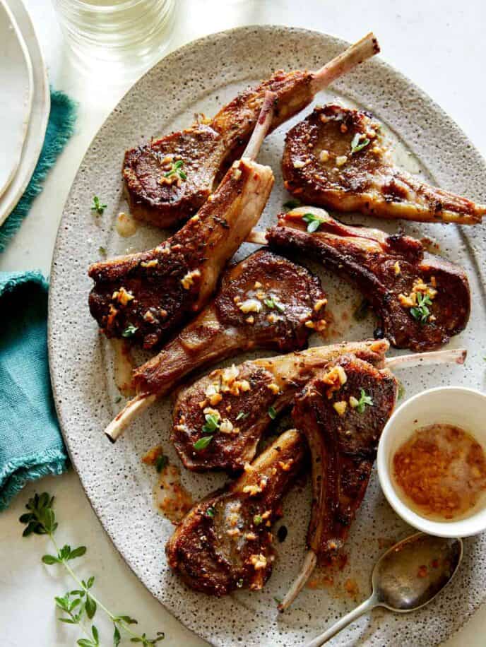 Garlic Butter Lamb Chops on a platter with a stack of plated next to it, a Valentine's dinner idea. 