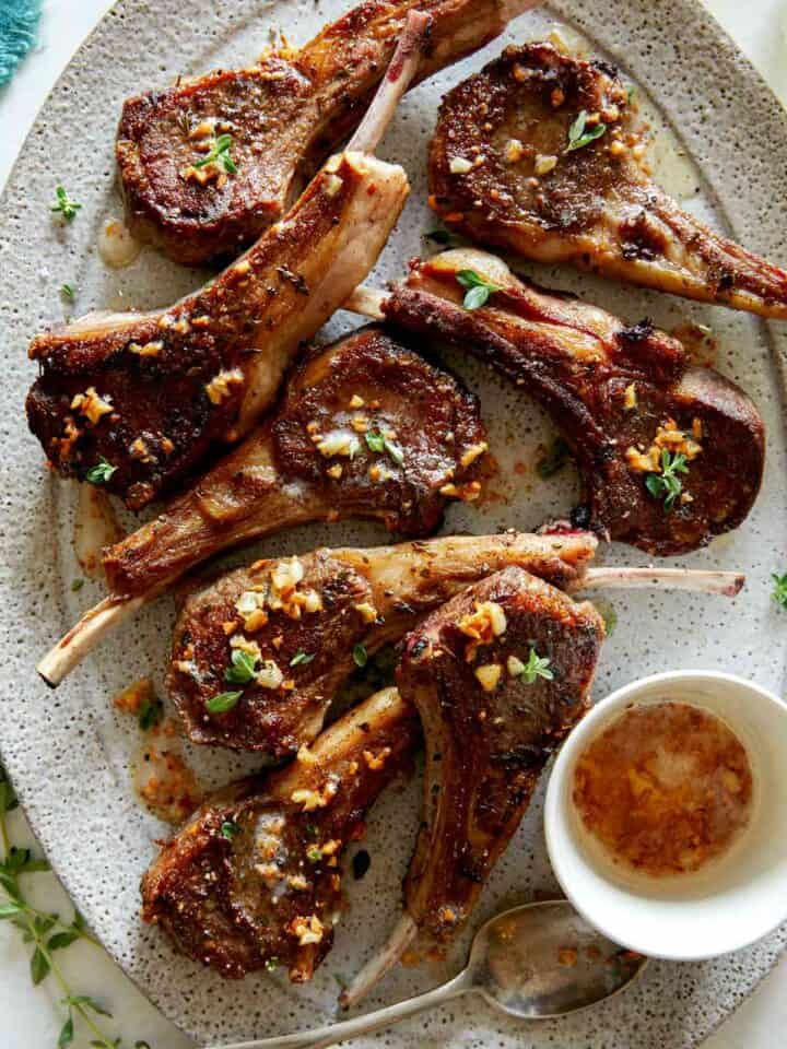 A platter of garlic butter lamb chops with a container on garlic butter next to them.