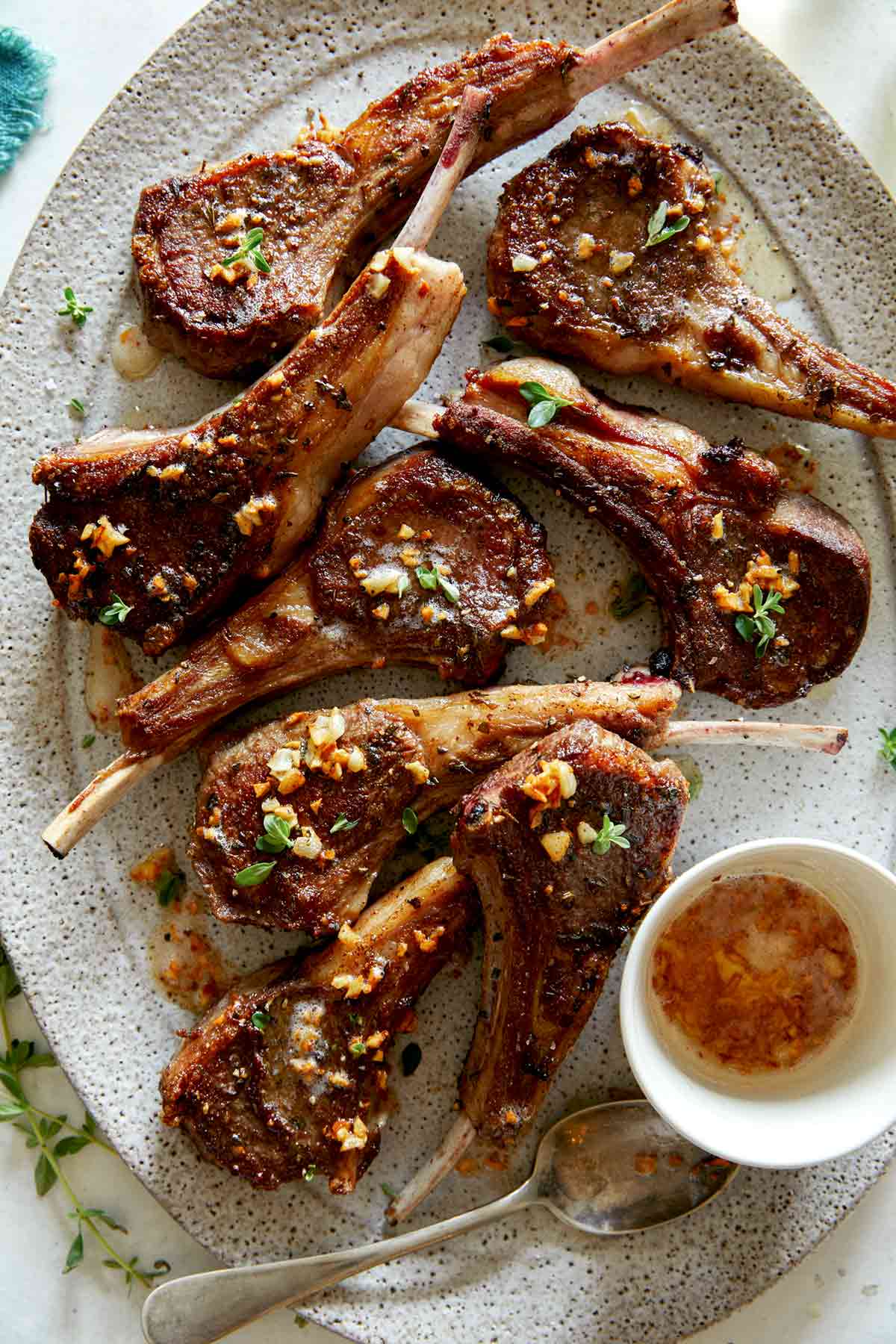 A platter of garlic butter lamb chops with a container on garlic butter next to them. 