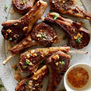 Close up on a platter of garlic butter lamb chops with a container on garlic butter next to them.