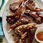 A platter of garlic butter lamb chops with a container on garlic butter next to them.
