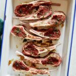 Marinated raw lamb chops in a dish on a kitchen counter.