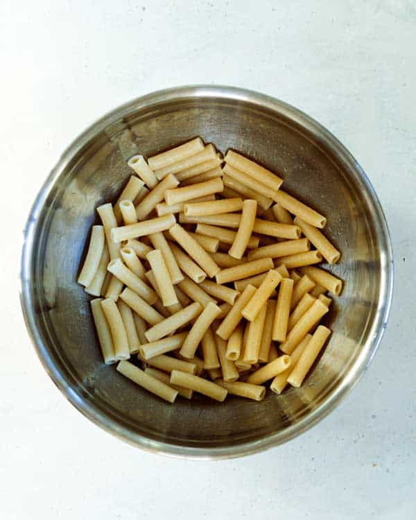 Cooked ziti pasta tossed with a little olive oil in a bowl.
