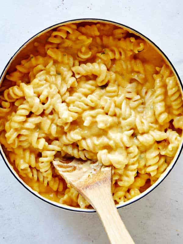 A close up on pumpkin mac and cheese in a pot with a wooden spoon.