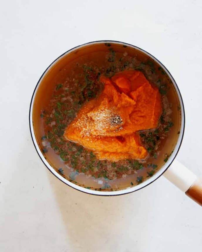 Adding Pumpkin Purée in a pot with other ingredients to make Pumpkin Soup.