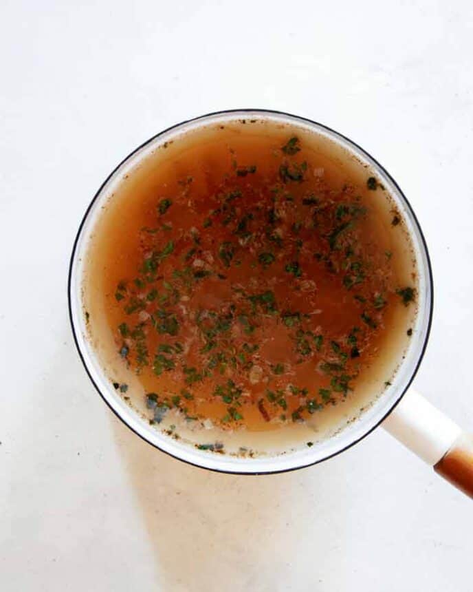 Adding stock to a pot with sautéd garlic, shallots and herbs for Pumpkin Soup.