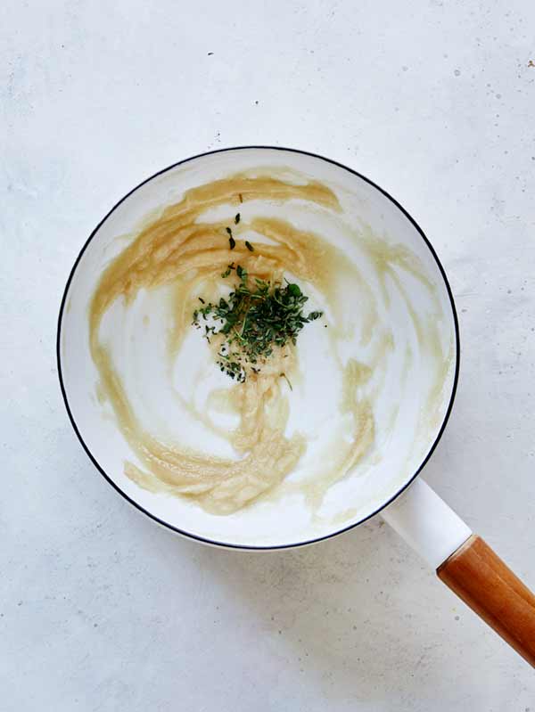 A cooked down roux with thyme being stirred in to make pumpkin mac and cheese.