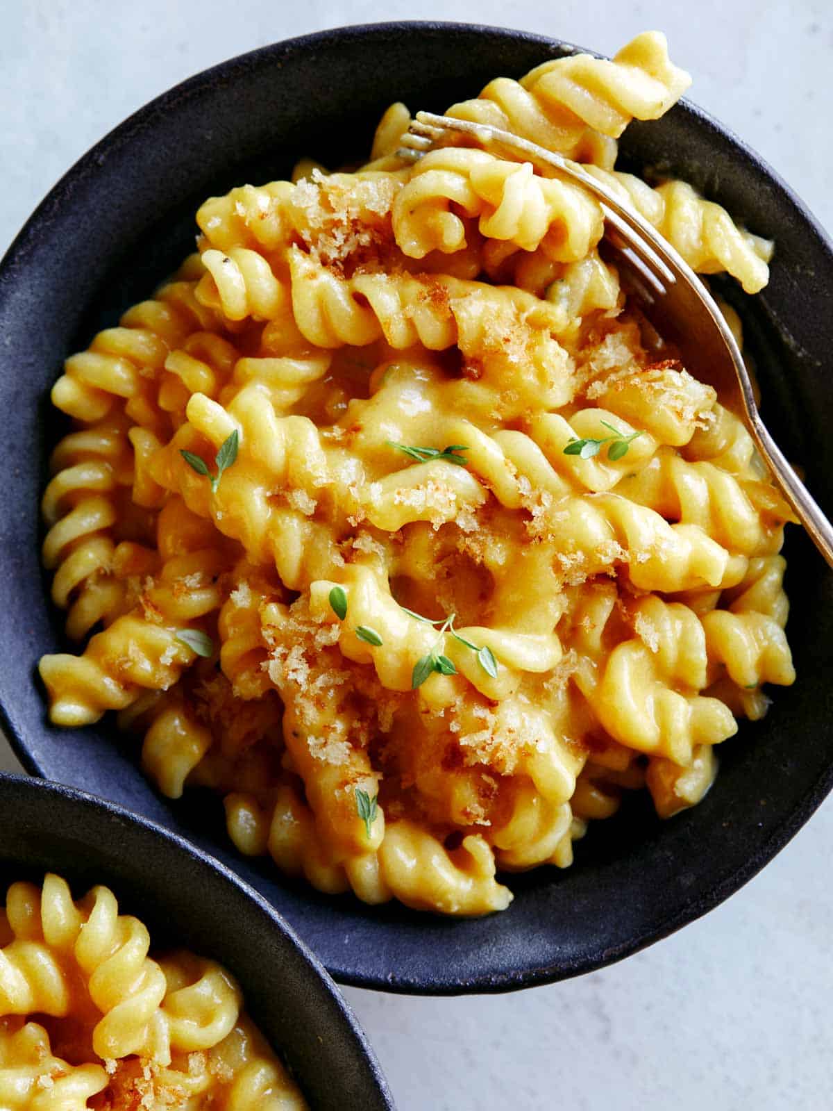 Two bowls of Pumpkin Mac and Cheese, and one with a fork in some of the pasta.