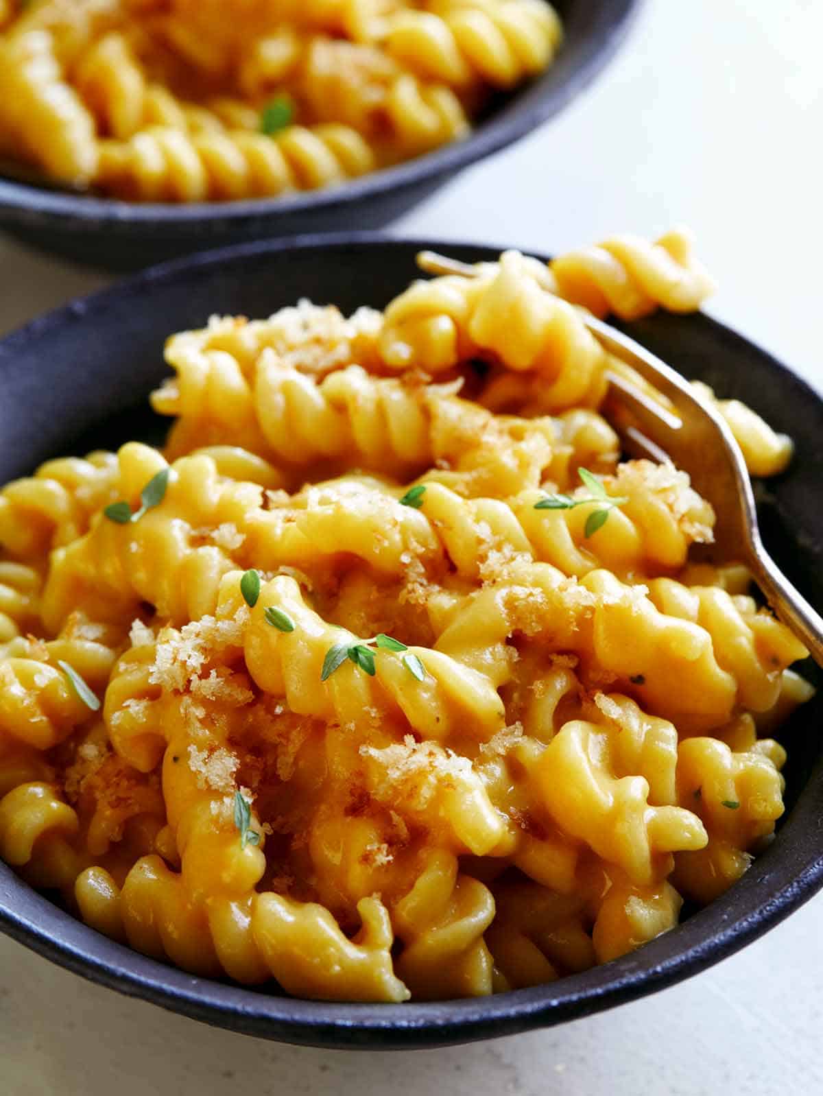 A bowl of Pumpkin Mac and Cheese with a fork spearing some pasta. 