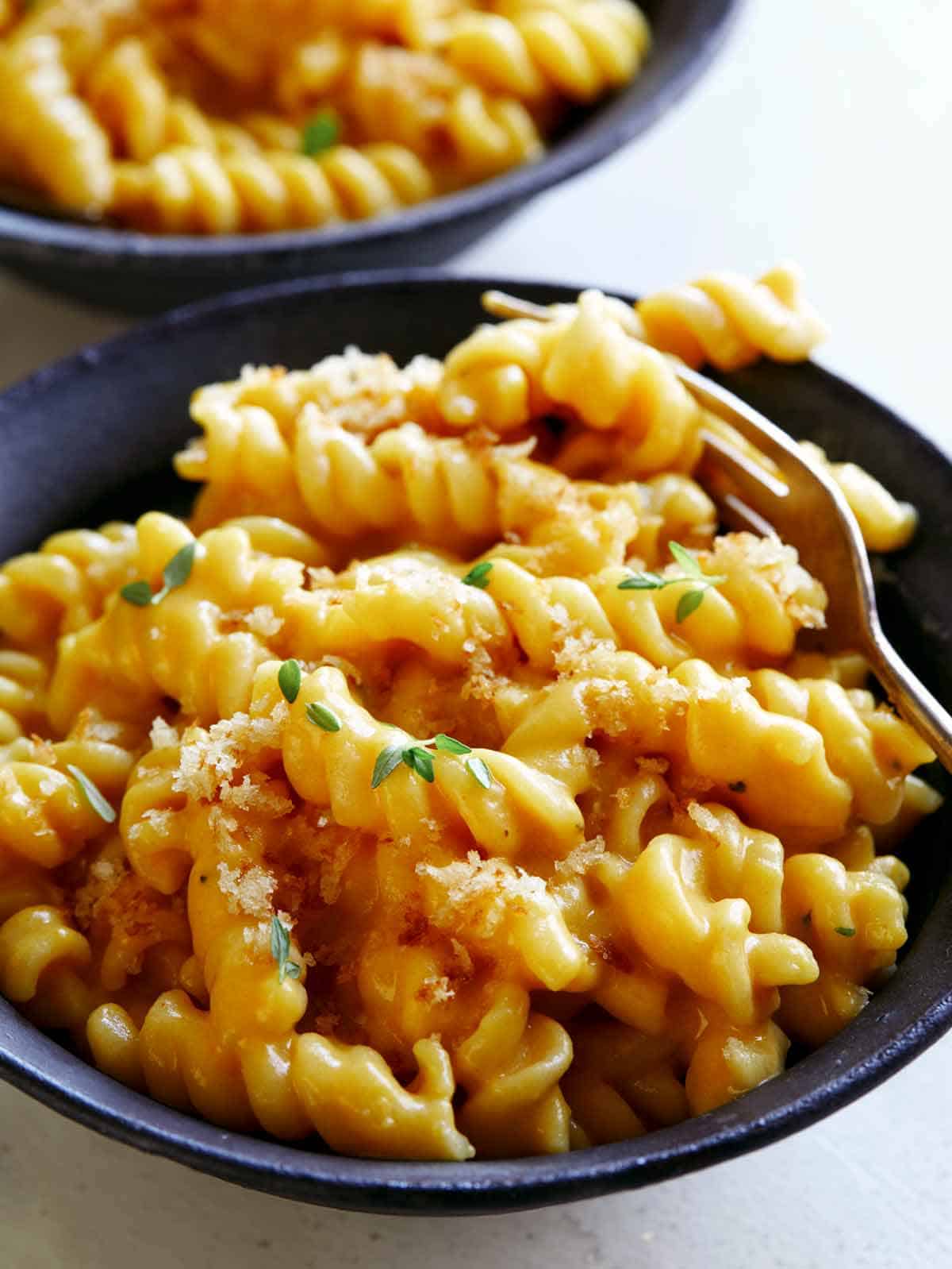 A bowl of Pumpkin Mac and Cheese with a fork spearing some pasta.
