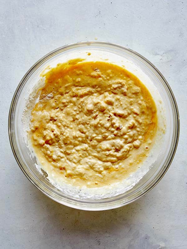 Mixed wet and dry ingredients for pumpkin pancakes in a glass bowl. 