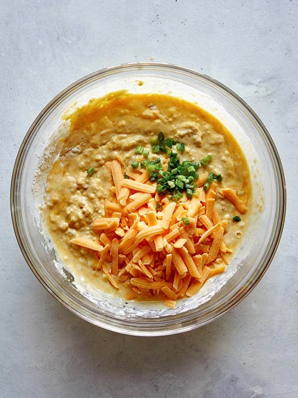 Cheese and green onions added to a pancake batter in a glass bowl. 