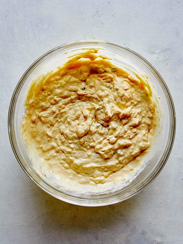 Cheese and green onions folded into pancake batter in a glass bowl.