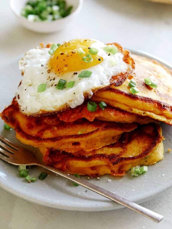 A plate of cheesy pumpkin pancakes with a egg on top of them. 