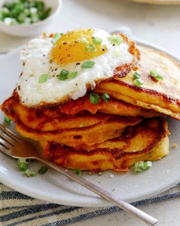 Cheesy Pumpkin Pancakes on a plate with a plate in the background of more pancakes.