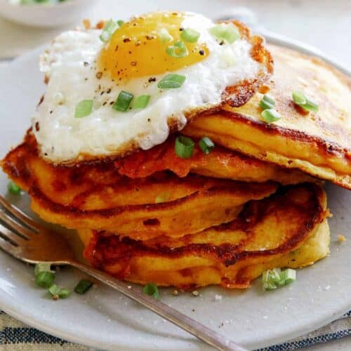 Cheesy Pumpkin Pancakes on a plate with a plate in the background of more pancakes.