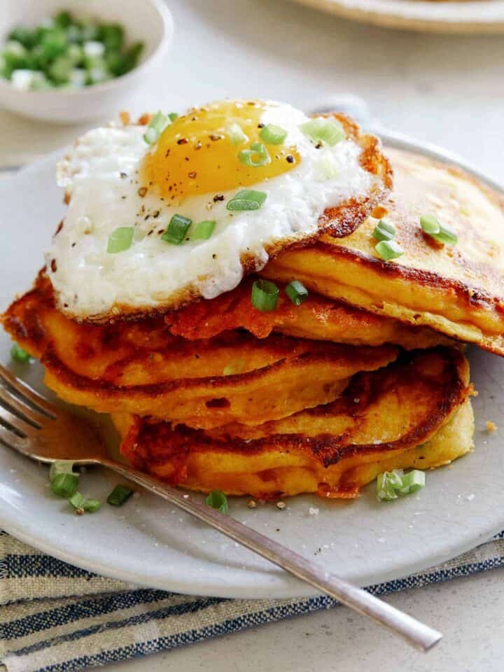 Cheesy Pumpkin Pancakes on a plate with a plate in the background of more pancakes.
