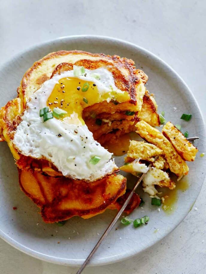 A plate of cheesy pumpkin pancakes with a fork digging into them. 