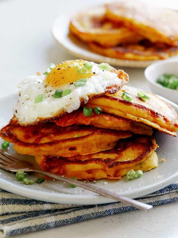 Cheesy Pumpkin Pancakes on a plate with a plate in the background of more pancakes. 