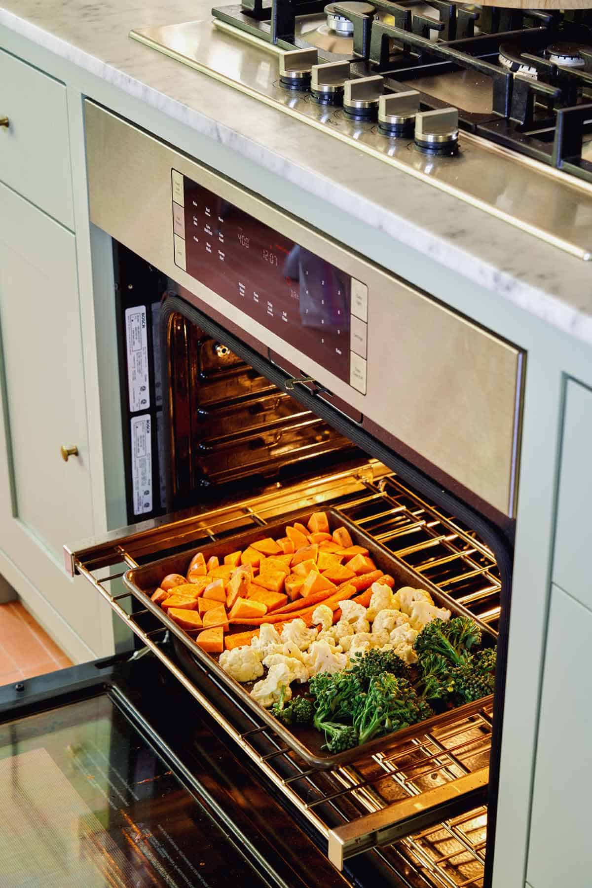 A sheet pan of vegetables going into an oven to roast. 