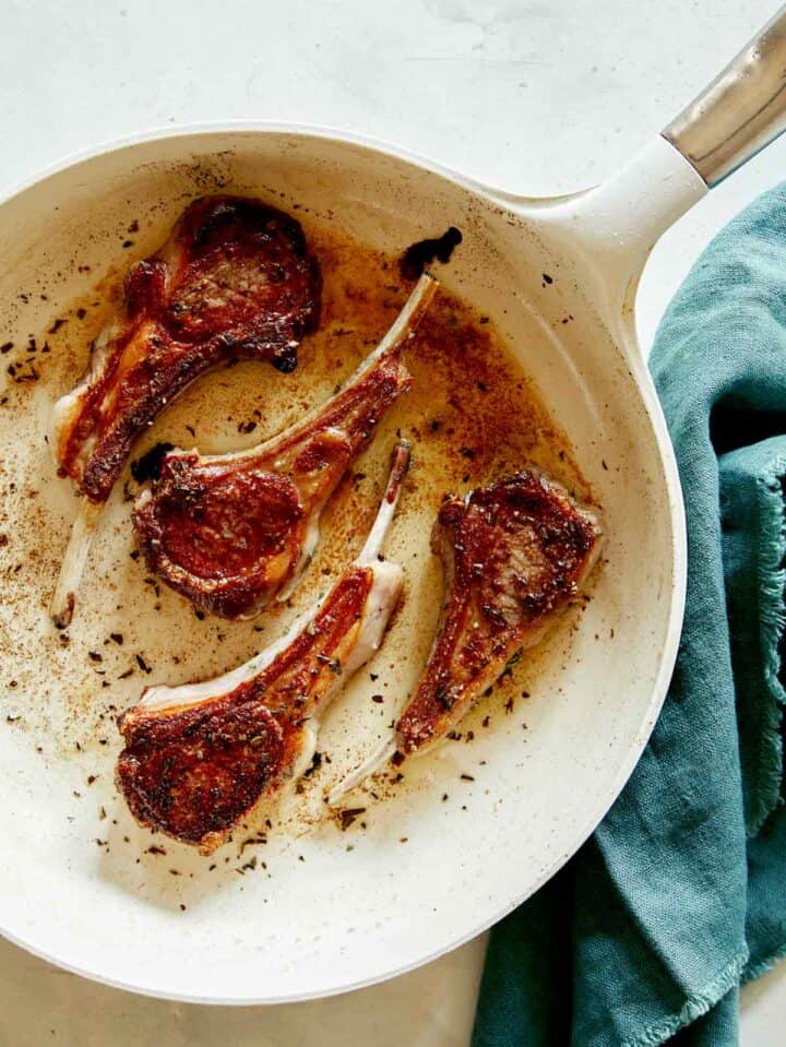 A skillet with freshly seared lamb chops in it.