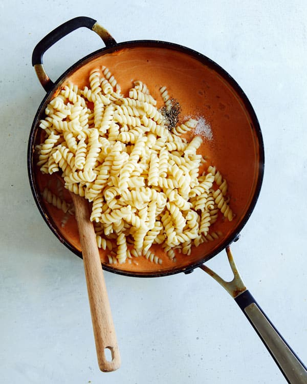 Pasta added to a skillet of vodka sauce with salt and pepper.