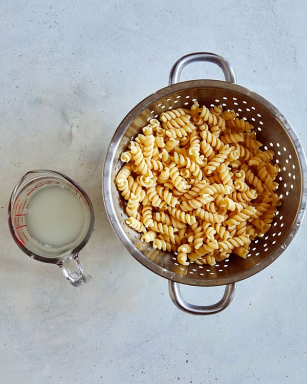 Pasta for Vodka Sauce in a collander with a measuring cup next to it full of reserved pasta water.