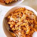 Two bowls of vodka sauce pasta with parmesan and a fork in it.