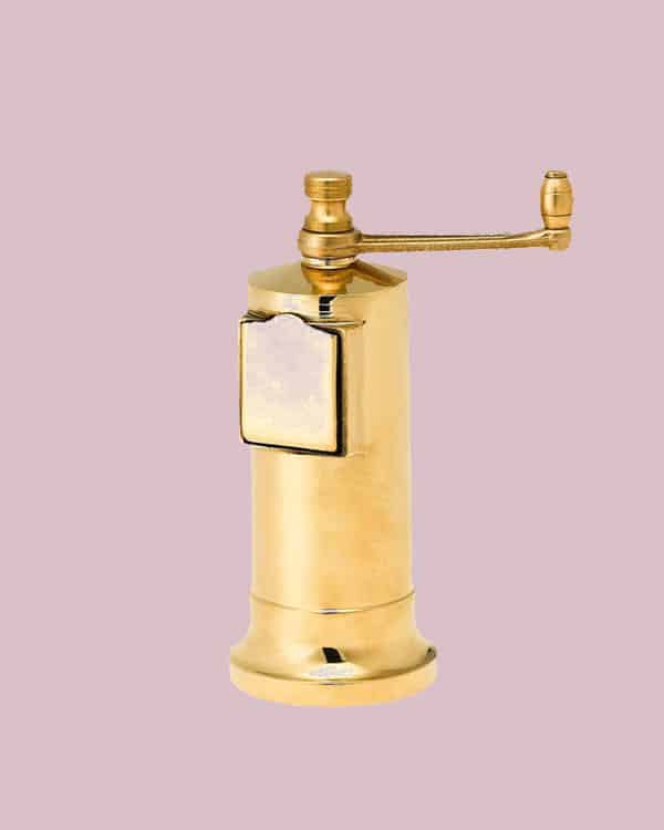 A brass pepper mill on a pink background.