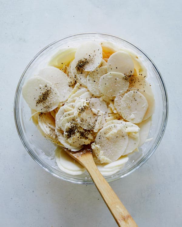 Thinly sliced potatoes in a bowl of cream.