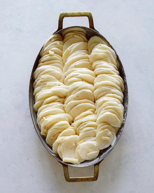 Thinly sliced potatoes in casserole dish to make potatoes gratin.