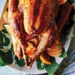 A citrus dry brined turkey on a platter with carving tools next to it.