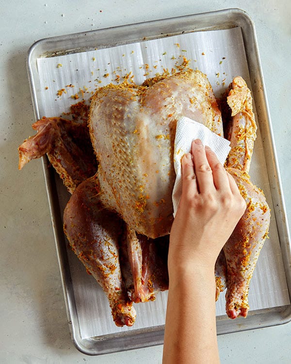 Wiping off a dry rub from a raw turkey on a baking sheet.