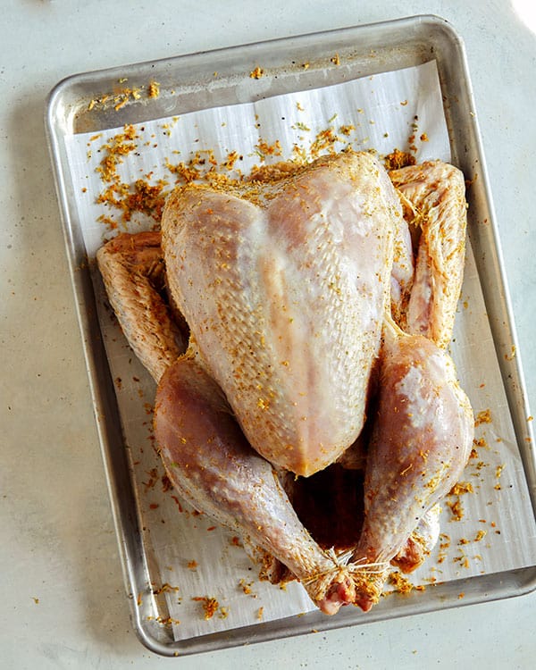 A raw turkey on a baking sheet with citrus dry brine. 