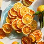 Dehydrated orange slices on a plate with some whole oranges next to it.